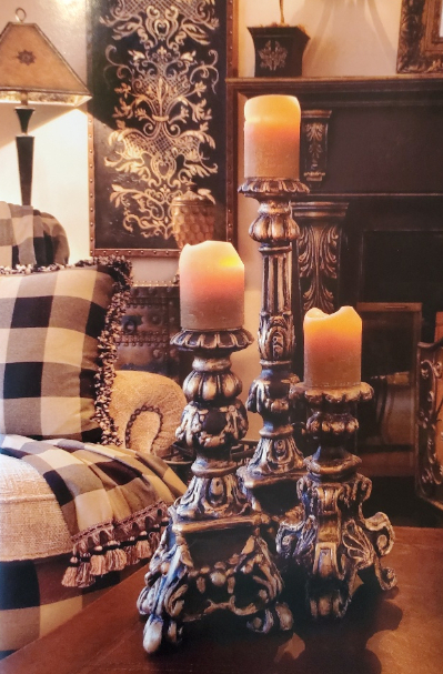 Ornate black and gold candlesticks with yellow candles, resting on a coffee table in an elegant living room.